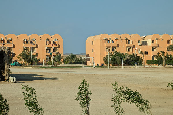 Beige clay buildings in the egyptian desert, three stories high, with laundry hanging on the balconies to dry